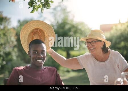 Glückliche Großmutter hält Strohhut über Enkel während Gartenparty An sonnigen Tag Stockfoto