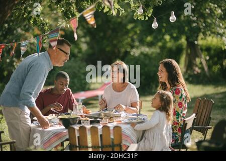 Älterer Mann und Enkelin sprechen beim Mittagessen mit der Familie Im Hinterhof während der Party Stockfoto