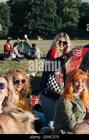 Lächelnde Freunde genießen einen Drink während des Campens am sonnigen Tag in Konzert Stockfoto