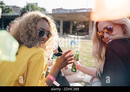 Lächelnde Freunde genießen Getränke, während sie im Rasen beim Konzert sitzen Stockfoto