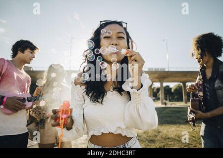 Frau bläst Seifenblasen, während Freunde spielen Ukulele während der Musik Ereignis Stockfoto