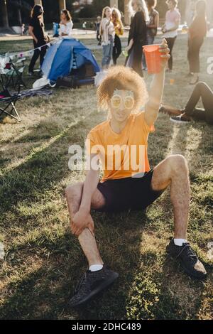 Portrait des Mannes, der während des Sitzens auf Gras trinkt Musikfestival Stockfoto