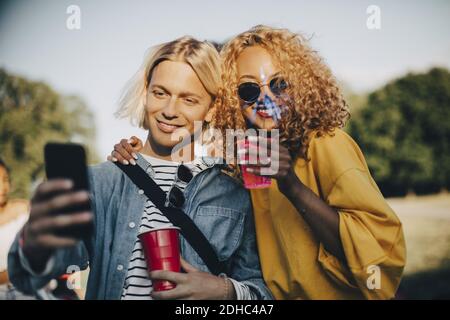 Lächelnder Mann nimmt Selfie mit Freund auf Smartphone, während Genießen Sie Getränke im Konzert Stockfoto
