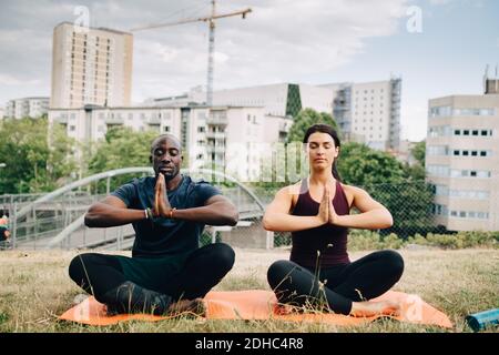Multiethnische Freunde üben Yoga auf dem Feld gegen Gebäude in der Stadt Stockfoto