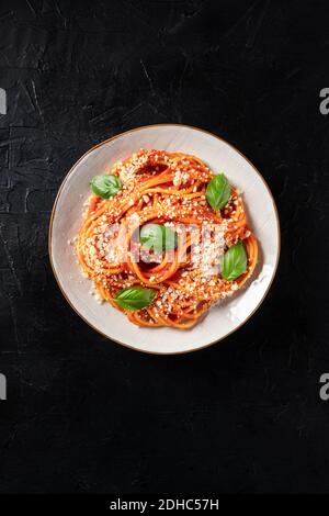 Spaghetti mit Tomatensauce, Parmesankäse und frischen Basilikumblättern, von oben auf dunklem Hintergrund geschossen Stockfoto