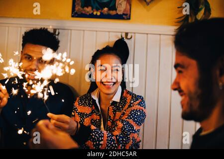 Fröhliche junge multiethnische Freunde sitzen mit brennenden Wunderkerzen im Restaurant Stockfoto