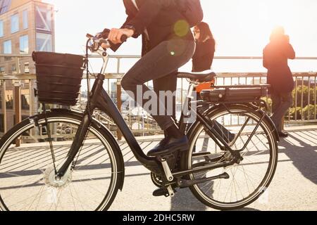 Niedriger Abschnitt der reifen Frau Reiten Elektro-Fahrrad von Pendlern Auf der Brücke in der Stadt gegen den Himmel Stockfoto