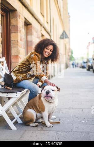 Lächelnde Frau, die mit Hund auf dem Bürgersteig in der Stadt sitzt Stockfoto