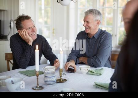 Fröhliche ältere Männer reden, während sie am Esstisch sitzen Stockfoto