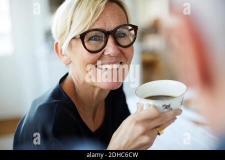 Lächelnd reife Frau hält Kaffeetasse, während weg zu schauen Zu Hause Stockfoto