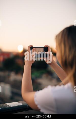 Zugeschnittenes Bild einer jungen Frau, die den Fernsehturm über ein Smartphone fotografiert Bei Sonnenuntergang Stockfoto