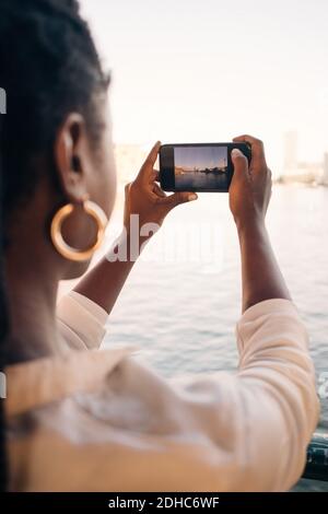 Zugeschnittenes Bild einer jungen Frau, die Fluss durch Smartphone fotografiert In der Stadt Stockfoto