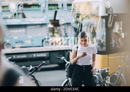 Junge Frau mit Handy, während sie an Fahrrädern steht Straße in der Stadt Stockfoto