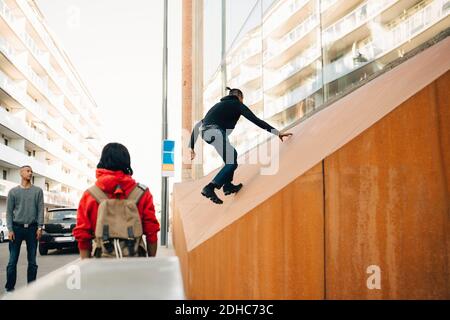 Freunde, die einen sorglosen Teenager beim Klettern an der Wand betrachten Stadt Stockfoto