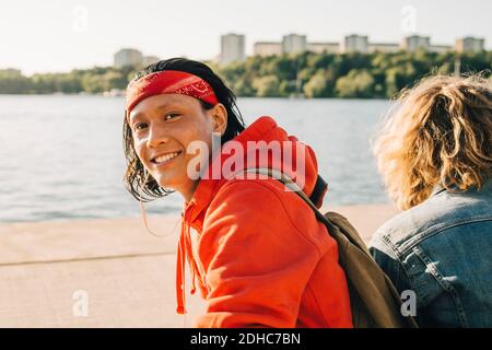 Porträt eines lächelnden jungen Mannes, der von einem Freund auf der Promenade sitzt An sonnigen Tagen Stockfoto