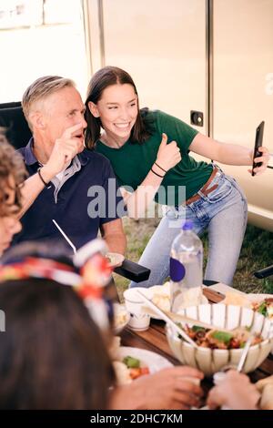 Teenager-Mädchen, Selfie mit Großvater auf Handy, während Essen auf dem Campingplatz Stockfoto