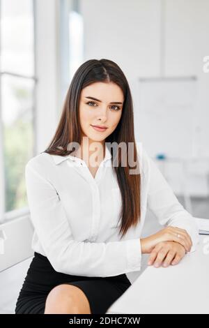 Porträt von lächelnd hübsche junge Geschäftsfrau sitzen am Arbeitsplatz Der Tisch im modernen Büro und Blick auf die Kamera Stockfoto