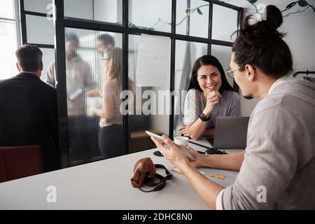 Männliche Unternehmer diskutieren mit lächelnden weiblichen Kollegen über digitale Tablette Am Schreibtisch im Büro Stockfoto