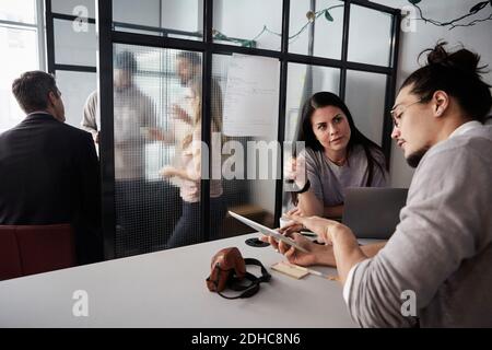 Geschäftsmann diskutiert weibliche Kollegin über digitale Tablet am Schreibtisch in Kreatives Büro Stockfoto