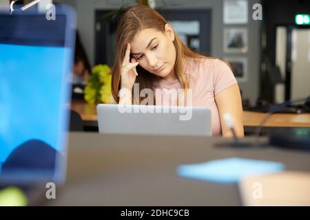 Angespannte kreative Geschäftsfrau, die im Büro auf den Laptop schaut Stockfoto