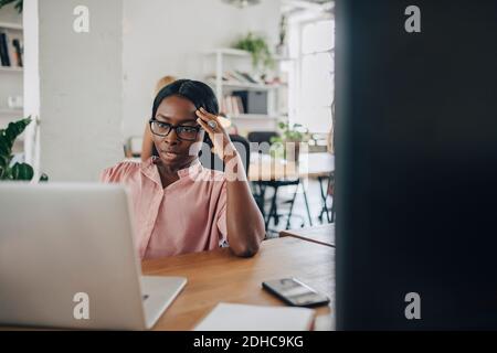 Angespannte junge Geschäftsfrau, die am Schreibtisch im Büro einen Laptop ansieht Stockfoto