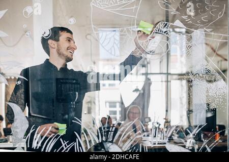 Lächelnd kreativ Geschäftsmann klebende Note auf gemustertem Glas in kleben Büro Stockfoto