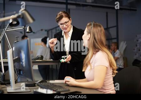 Kreative Geschäftsfrau mit Blick auf weibliche Bankmanagerin, die Solarspielzeug hält Auto im Kreativbüro Stockfoto