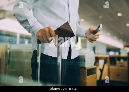 Mittelteil des Geschäftsmannes mit Pass und Smartphone am Flughafen Stockfoto