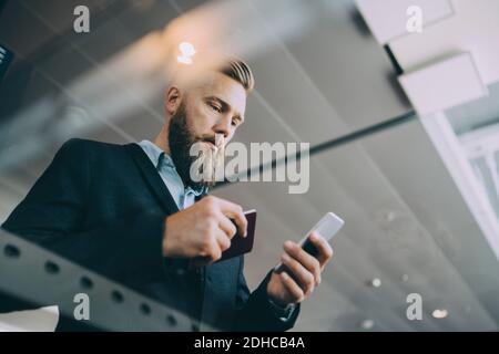 Niedriger Winkel Ansicht des Geschäftsmannes mit Smartphone während halten Reisepass am Flughafen Stockfoto