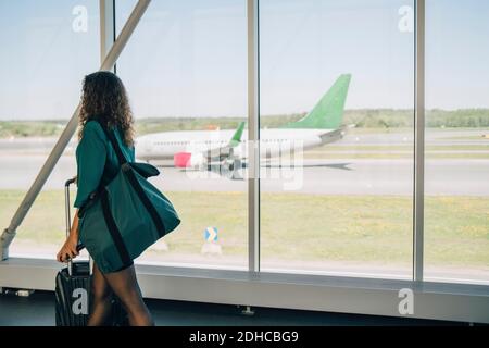 Geschäftsfrau, die mit dem Gepäck am Fenster auf dem Flur am Flughafen herumläuft Stockfoto