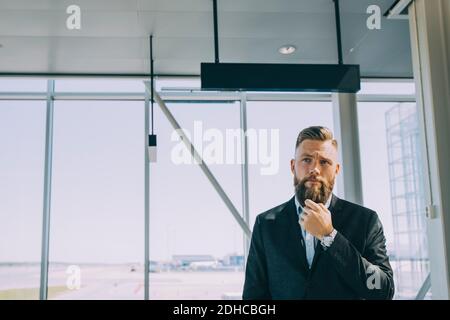 Nachdenklicher Geschäftsmann, der am Flughafen gegen das Fenster steht Stockfoto