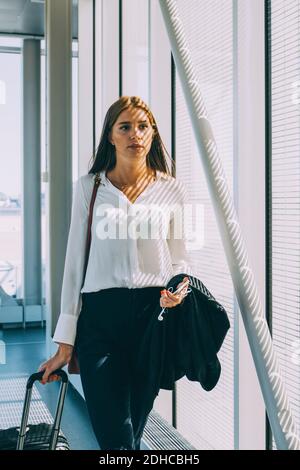 Junge Geschäftsfrau zieht Gepäck, während sie im Korridor am Flughafen läuft Stockfoto