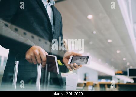 Mittelteil eines mittelerwachsenen Geschäftsmannes mit Pass und Smartphone Am Flughafen Stockfoto