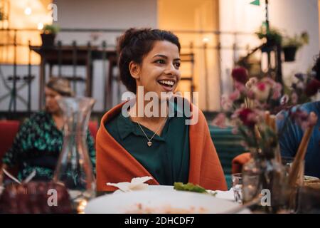 Lächelnde junge Frau, die wegschaut, während sie am Tisch sitzt Dinnerparty Stockfoto