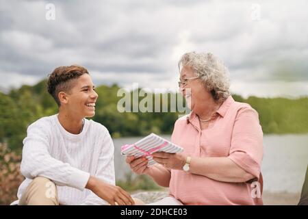 Fröhliche Großmutter, die dem Enkel im Park am Seeufer das Geschenk gibt Während des Picknicks Stockfoto