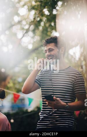 Glücklicher junger Mann, der durch Kopfhörer spricht, während er auf dem Balkon steht Während der Party Stockfoto