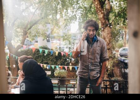 Junger Mann, der auf dem Balkon steht und mit dem Handy spricht Während der Party Stockfoto