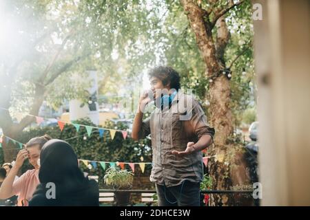Der junge Mann gestikuliert, während er auf dem Balkon mit dem Handy spricht Während der Party Stockfoto