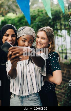 Glückliche multiethnische Freundinnen nehmen Selfie über Handy in Hinterhof Stockfoto