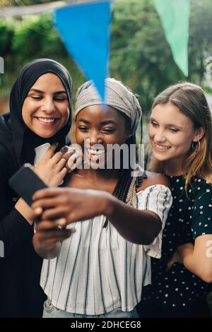 Glückliche multiethnische Freundinnen nehmen Selfie über Smartphone in Hinterhof Stockfoto