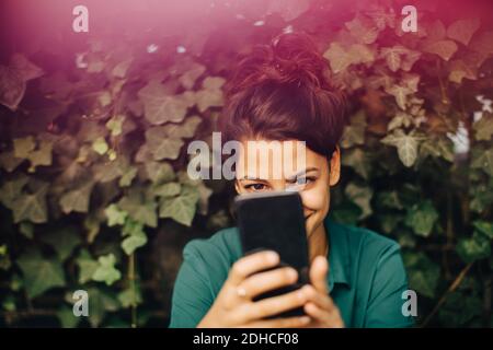 Lächelnde junge Frau, die im Hinterhof durch das Handy fotografiert Stockfoto