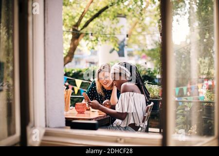 Multiethnische Freundinnen, die durch das Fenster auf das Mobiltelefon schauen Stockfoto