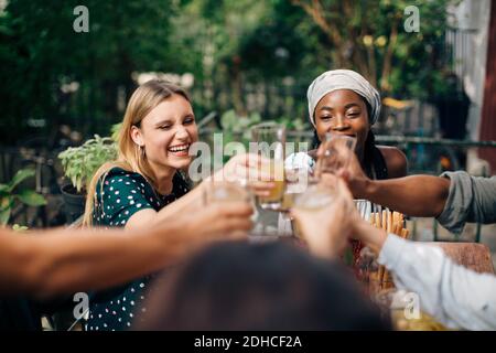 Multiethnische Freunde, die auf dem Balkon sitzen und Getränke toasten Stockfoto