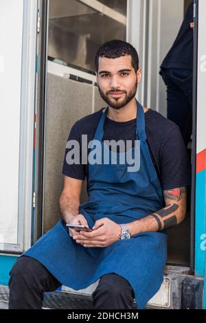 Porträt von selbstbewussten jungen männlichen Unternehmer sitzen mit Smartphone Am Eingang des Foodtrucks Stockfoto