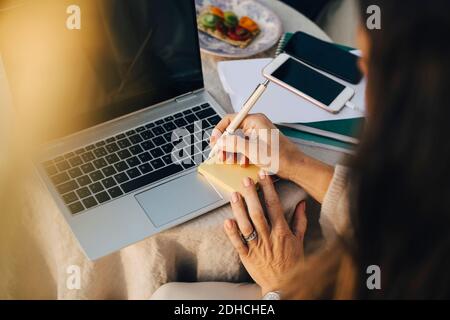 Cropped Frau schreiben auf Klebenote über Laptop am Tisch Stockfoto