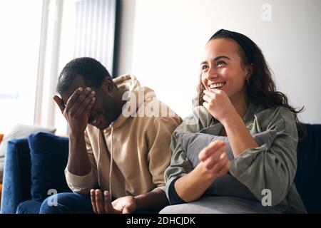 Junge gemischte Ethnizität Paar kringend beim Essen Popcorn auf dem Sofa Zu Hause, um gemeinsam Filme auf dem fernseher anzusehen oder zu streamen Stockfoto