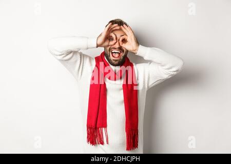 Happy guy feiert weihnachten, zeigt lustige Gesichter und lachen, stand über weißem Hintergrund im Winter Pullover und rote Narbe Stockfoto