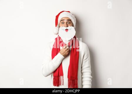 Weihnachtsfeier und Feier Konzept. Lustige junge Mann in Santa Hut hält weißen Bart Maske und macht Gesichter, genießen New Ye Stockfoto