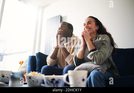 Aufgeregt und angespannt junge gemischte Ethnizität Paar auf dem Sofa sitzen Zu Hause Sportereignisse im fernsehen anschauen oder streamen Stockfoto