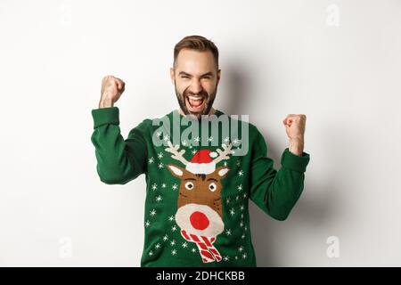 Neujahr, Feiertage und Feier. Aufgeregt bärtigen Mann in Weihnachten Pullover, so dass Faust Pumpen und schreien vor Freude, jubeln Stockfoto